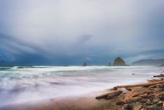 the beach is covered in rocks and water as storm clouds loom over it on an overcast day