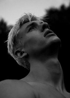 black and white photograph of a man with blonde hair looking up to the sky in front of trees