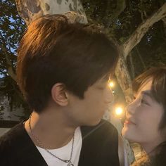 a man and woman standing next to each other near a tree with lights in the background