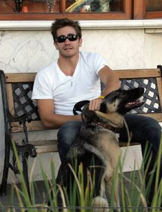 a man sitting on a bench with his dog in front of him and wearing sunglasses