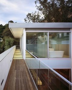 a long wooden walkway leading to a white building with glass walls and doors on both sides