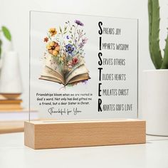 an open book sitting on top of a table next to a plant and potted cactus