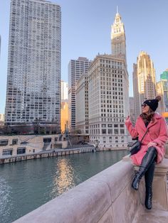 a woman sitting on the edge of a bridge in front of some buildings and water