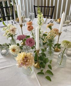 a table topped with lots of vases filled with flowers next to tall white candles