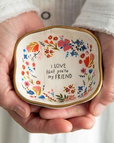 a person holding a small bowl with flowers on it that says i love you're my friend