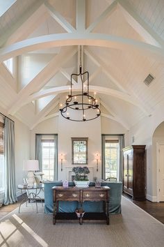 a living room filled with furniture and a chandelier hanging from the vaulted ceiling