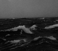 black and white photograph of waves in the ocean on a gloomy day with an airplane flying overhead