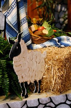 a sheep figurine sitting on top of hay next to a basket of fruit