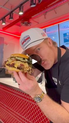 a man is eating a large sandwich in a fast food restaurant while wearing a hat