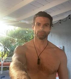 a shirtless man with no shirt on standing in front of a pool and looking at the camera