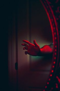 a person's hand reaching out from behind a mirror in a dark room with red lighting