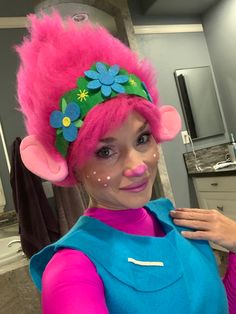 a woman with pink hair wearing a blue shirt and flowered headpiece in a bathroom