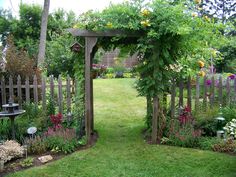 a garden with lots of plants and flowers on the grass, surrounded by a wooden fence