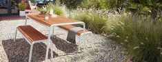 a wooden table sitting on top of a gravel covered ground next to tall grass and trees