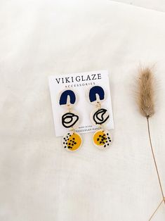 a pair of earrings sitting on top of a white sheet next to a dried plant