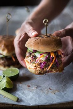 a person is holding a hamburger with toothpicks in their hands and some sliced limes on the side