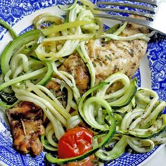 a blue and white plate topped with chicken, zucchini noodles and tomato slices