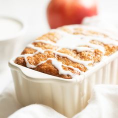 a loaf of cinnamon apple bread with icing in a white dish next to an apple