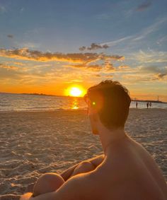 a man is sitting on the beach watching the sun go down over the water and people in the distance