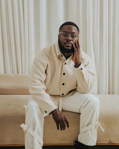 a man sitting on top of a couch next to a white curtained window sill