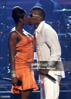 two people kissing each other on stage with lights in the background and one person wearing an orange dress