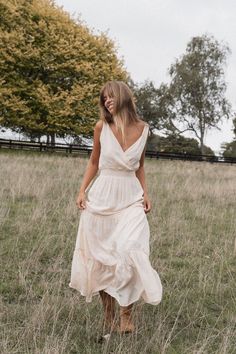 a woman in a white dress is walking through the grass