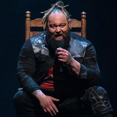 a man with dreadlocks sitting on a chair holding a microphone in his hand