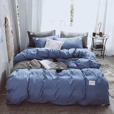 a bed with blue sheets and pillows in front of a window