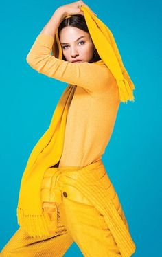 a woman in yellow is posing with her arms behind her head and hands on her head