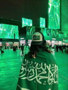 a person wearing a hat and green shawl standing in front of large screen displays