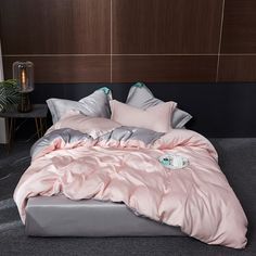 a bed with pink sheets and pillows in a room next to a plant on the floor