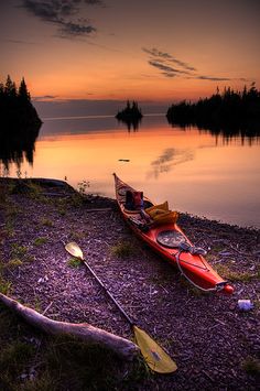 a red kayak sitting on the shore of a lake