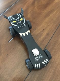 a black toy car with yellow eyes and fangs on it's face sitting on a wooden floor