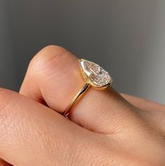 a woman's hand holding a yellow gold ring with a pear shaped diamond on it