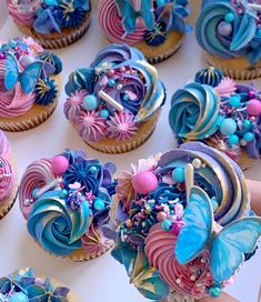 cupcakes decorated with blue, pink and purple icing are being held by someone's hand