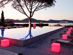 an outdoor swimming pool with lounge chairs and lights on the ground near it at dusk