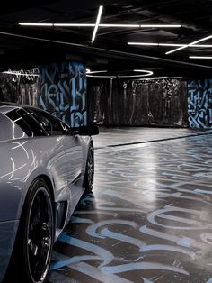 a car parked in a parking garage with graffiti on the floor and walls behind it