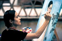 a woman is painting on an easel with her hand and looking at the viewer