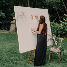 a woman standing in front of an easel holding a drawing on it's side