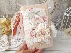 a hand holding a card with flowers and lace on it, next to a birdcage