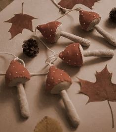 some little mushrooms and leaves are hanging from strings on a table with pine cones, acorns, and twine