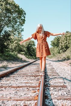 a woman is standing on train tracks with her arms out and she's wearing an orange dress