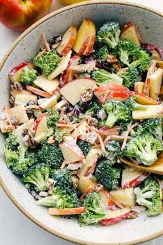 a bowl filled with broccoli and apples next to an apple on the table