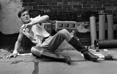 a man sitting on the ground in front of a brick wall