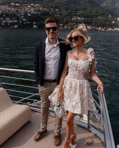 a man and woman standing on the deck of a boat in front of some water