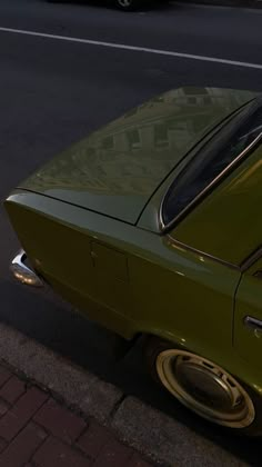 an old green car is parked on the side of the road next to a curb