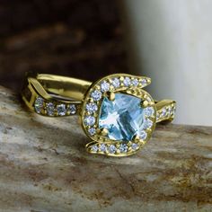 an engagement ring with blue topazte and white diamonds on a stone slab in front of a waterfall