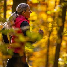 an older woman jogging through the woods in autumn