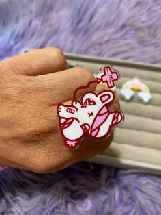 a person's hand with a pink and white elephant ring on top of it