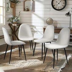 four white chairs sitting in front of a clock on a wall next to a rug